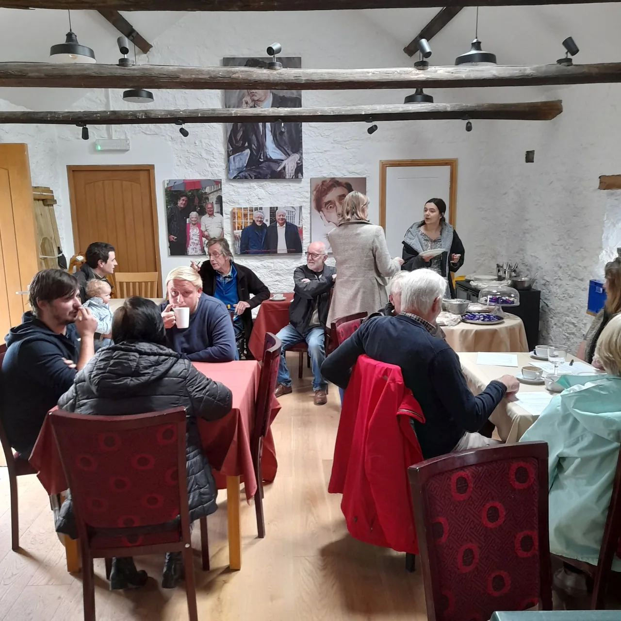 People chatting over tea inside the stone-walled Hub & Café, beneath exposed timber beams