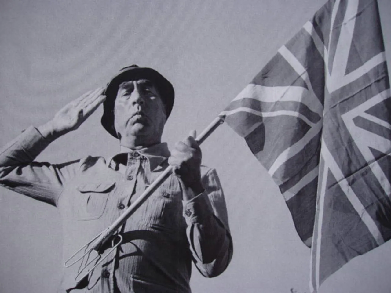 Frankie Howerd saluting beside the Union flag