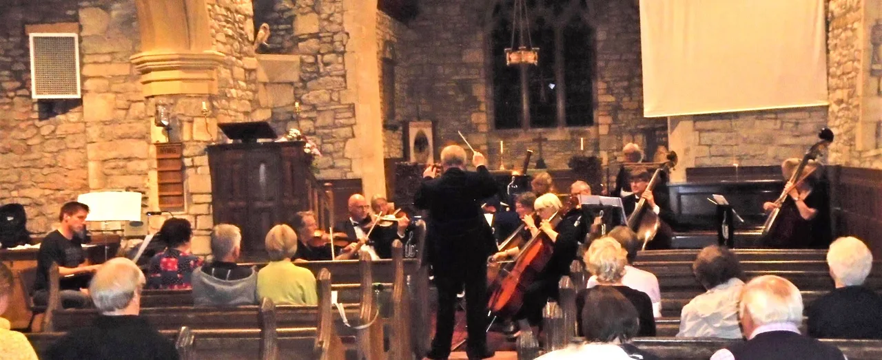 An orchestra performing for a seated audience inside a stone church